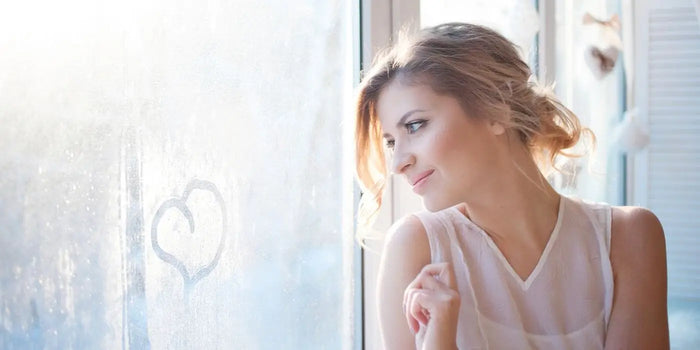 Femme portant une coiffure romantique, traçant un cœur sur une vitre.