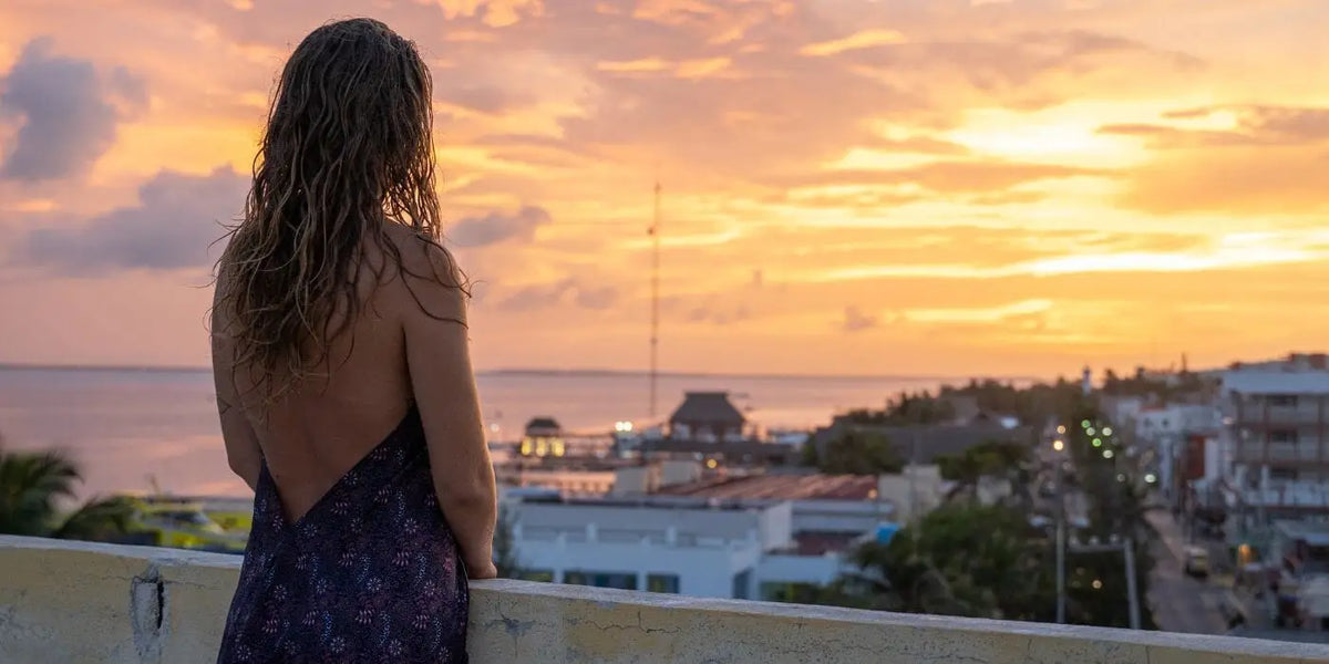 Femme portant une robe dos nu face à un coucher de soleil.