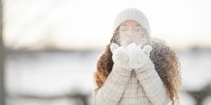Femme qui souffle de la neige dans ses mains.