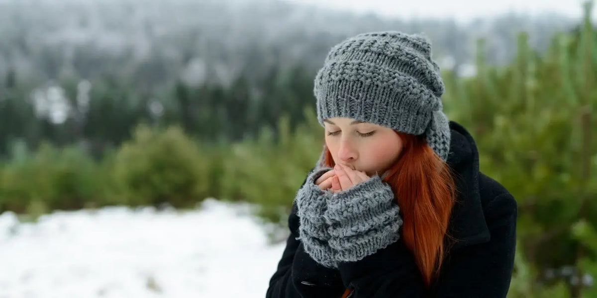 Femme portant un bonnet qui se réchauffe les mains en soufflant dessus.