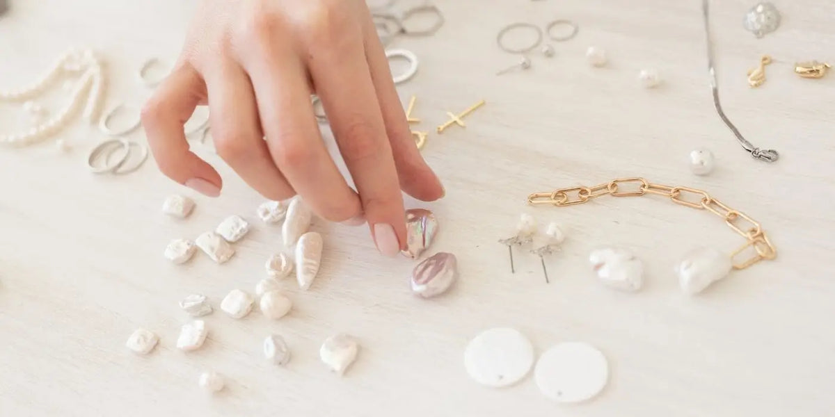 Main qui sélectionne des pendentifs pour réaliser un collier de dos.