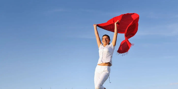 Une femme tient une écharpe rouge qui vole derrière elle.