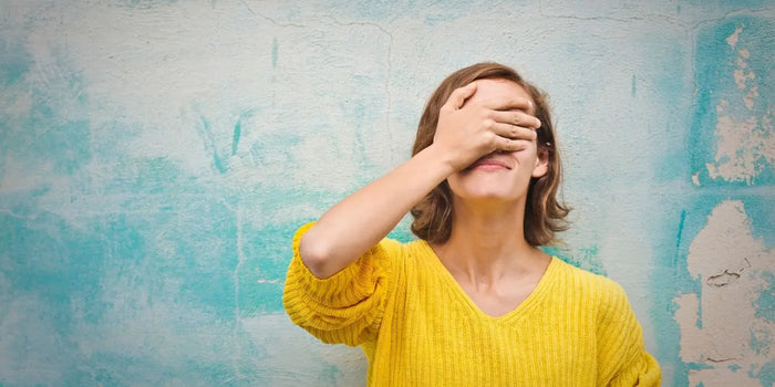 Femme avec une main posée sur le visage devant un mur bleu.