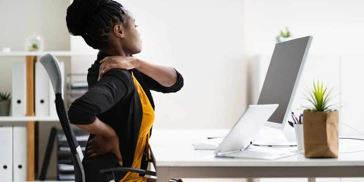 Femme souffrant d'un mal de dos face à son bureau.
