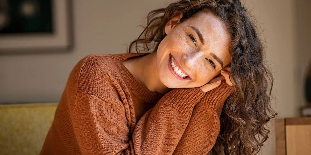 Femme souriante portant un pull couleur rouille.