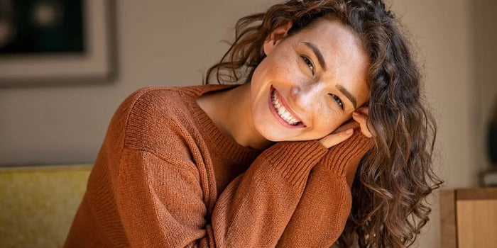 Femme souriante portant un pull couleur rouille.