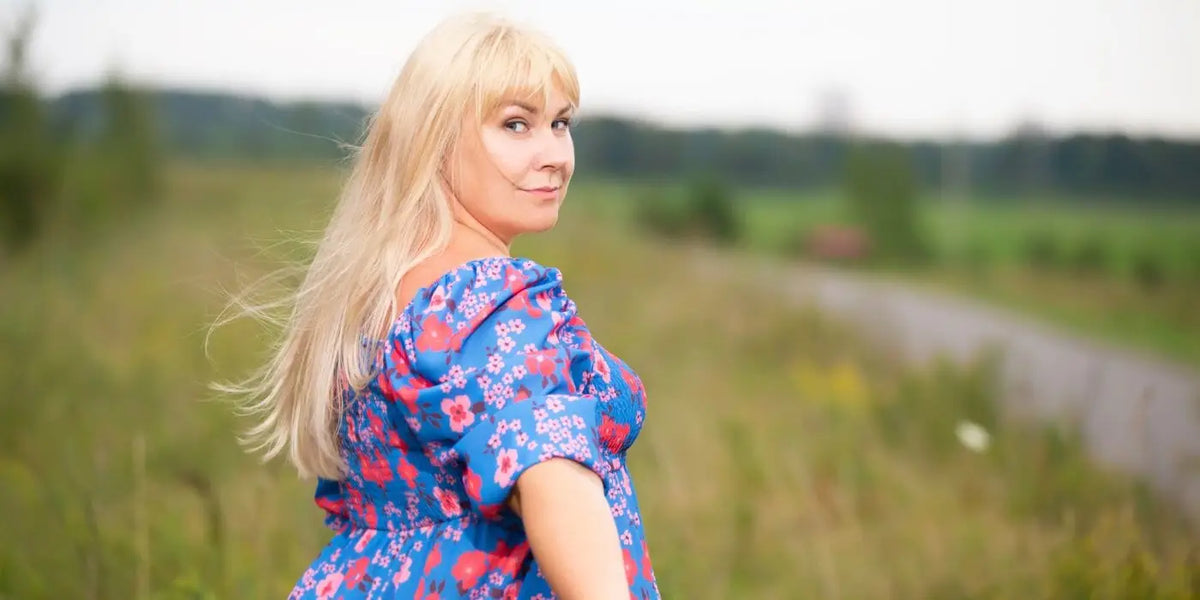 Femme blonde portant une robe à fleurs dans des champs de blé.