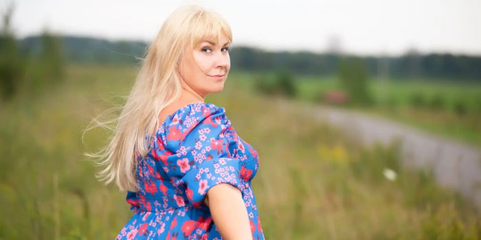 Femme blonde portant une robe à fleurs dans des champs de blé.