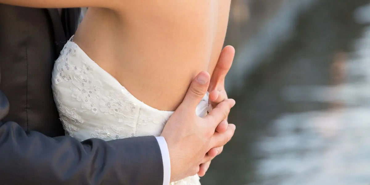 Femme en robe de mariée dos nu, dans les bras de son mari.