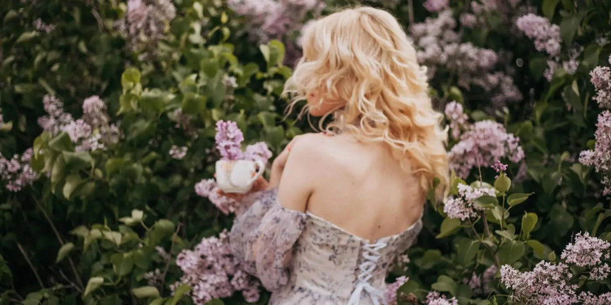 Femme portant une robe dos nu devant un lilas en fleur.