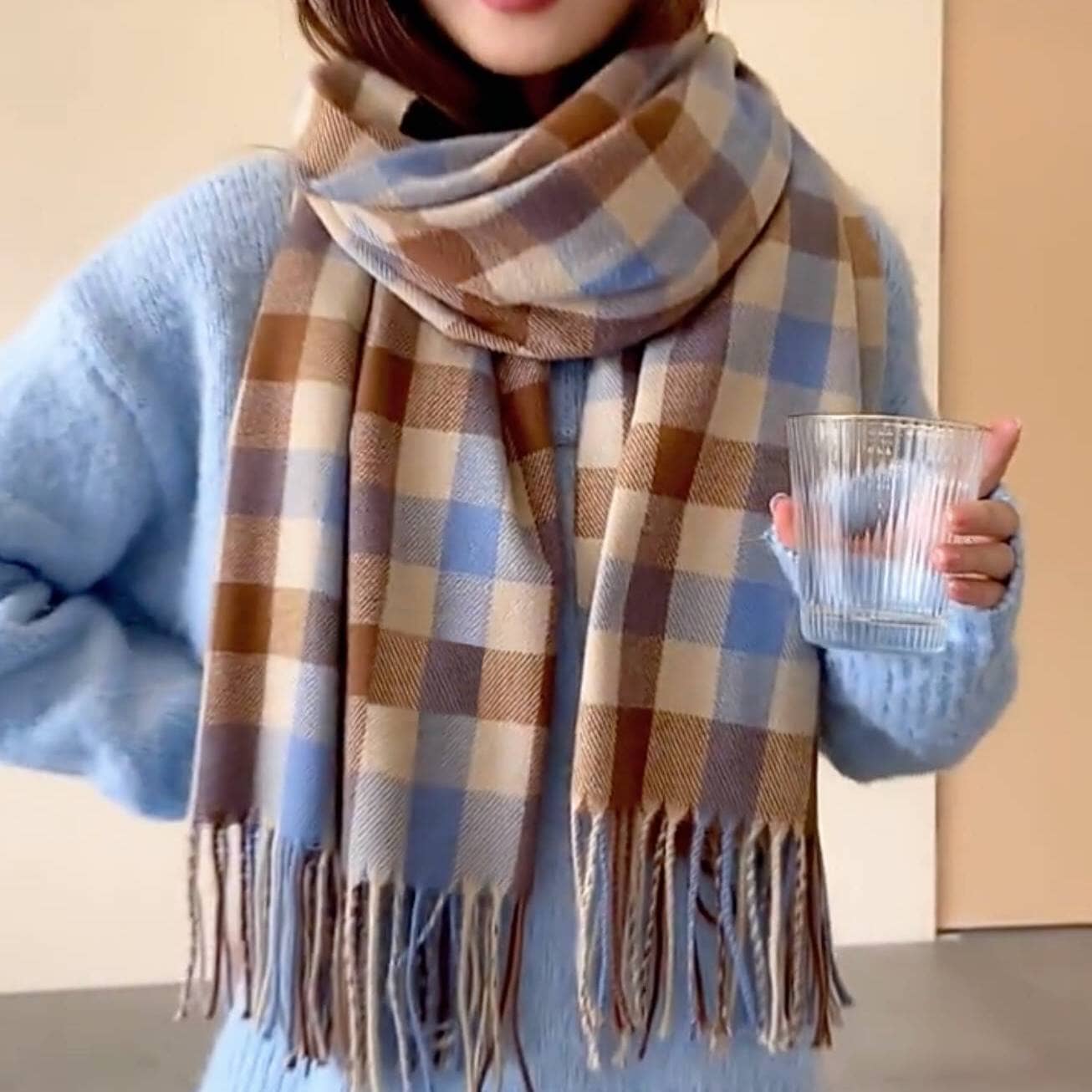 Echarpe à carreaux en cachemire aux tons bleus et marrons portée par une femme portant un pull en laine bleue et tenant un verre en cristal.