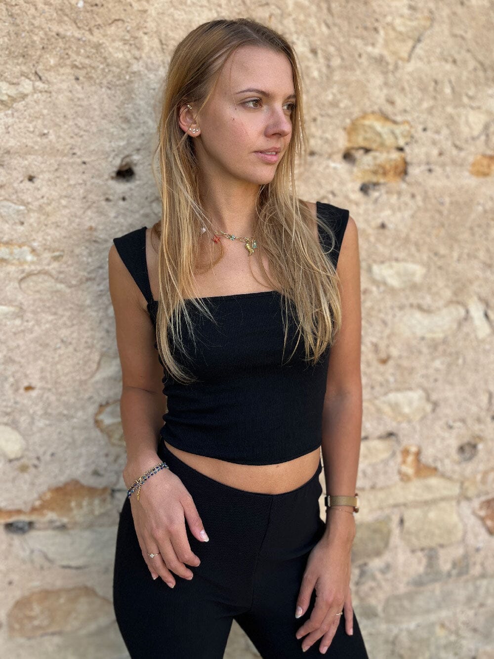 femme portant un débardeur noir col carré crop top tatiana avec un short en jean clair devant un mur blanc et un cactus