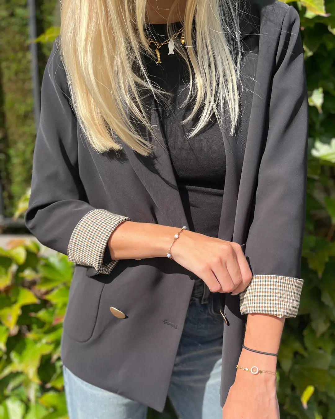 Veste blazer femme noire élégante portée avec jeans, manches retroussées à motif, idéale pour un look chic décontracté.