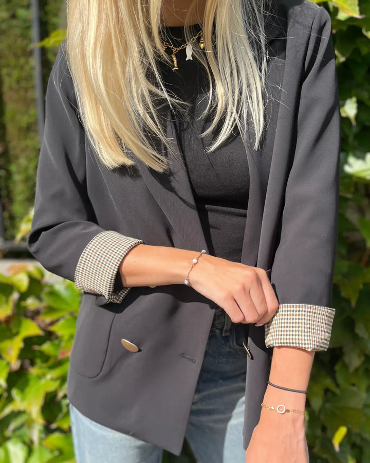 Veste blazer femme noire élégante portée avec jeans, manches retroussées à motif, idéale pour un look chic décontracté.