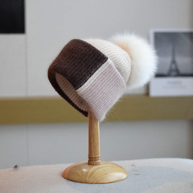 bonnet à pompon coline en tricot bicolore marron et beige avec un grand pompon blanc exposé sur un support en bois