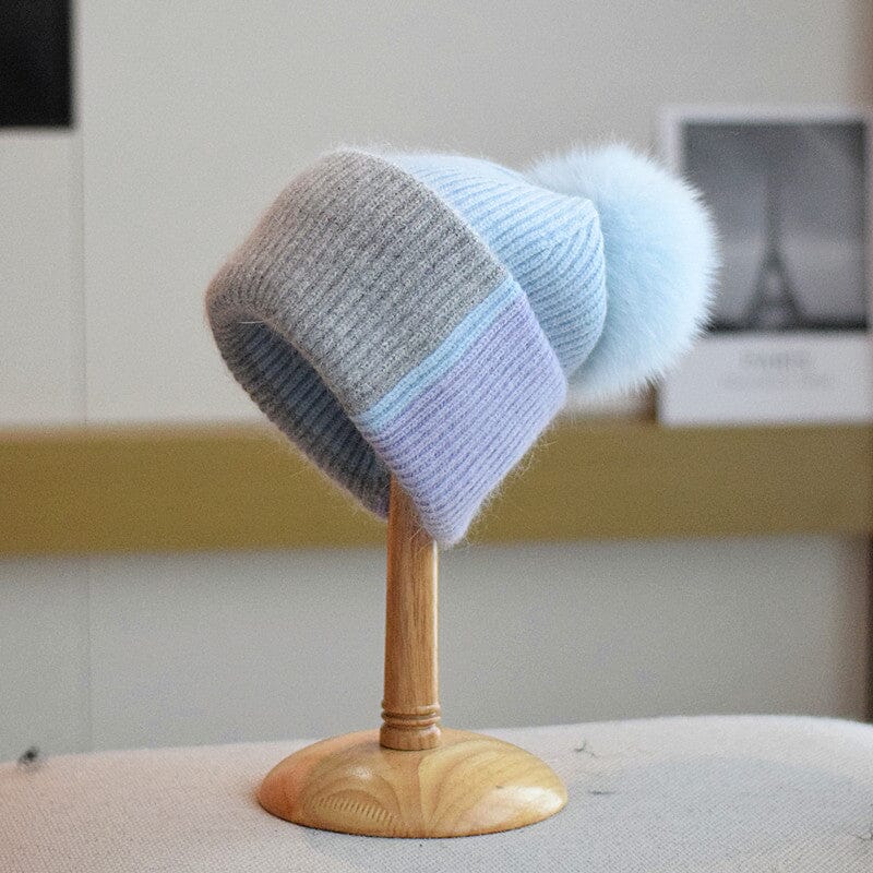 bonnet à pompon coline gris et bleu en laine avec grosse boule, présenté sur un présentoir en bois dans un intérieur clair