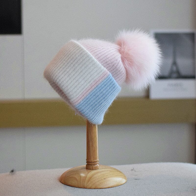 bonnet à pompon pastel coline en laine tricotée pour enfant posé sur un présentoir en bois dans un intérieur cosy