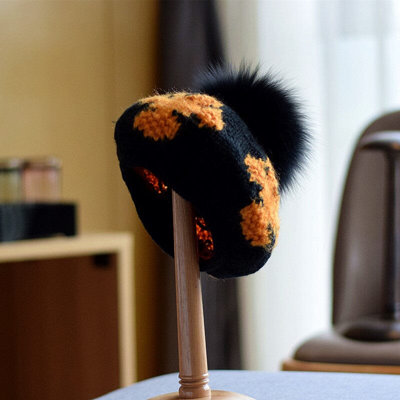 bonnet béret en laine noire et orange avec pompon en fourrure noire, modèle miriam sur support exposé en intérieur