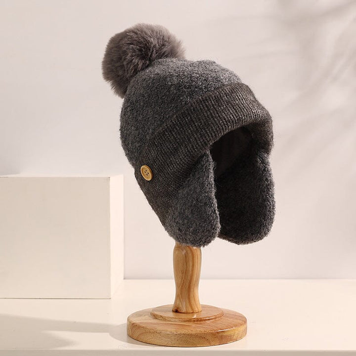Bonnet cache-oreille en laine pour femme avec pompon et bouton en bois, modèle nina, exposé sur un présentoir bois.