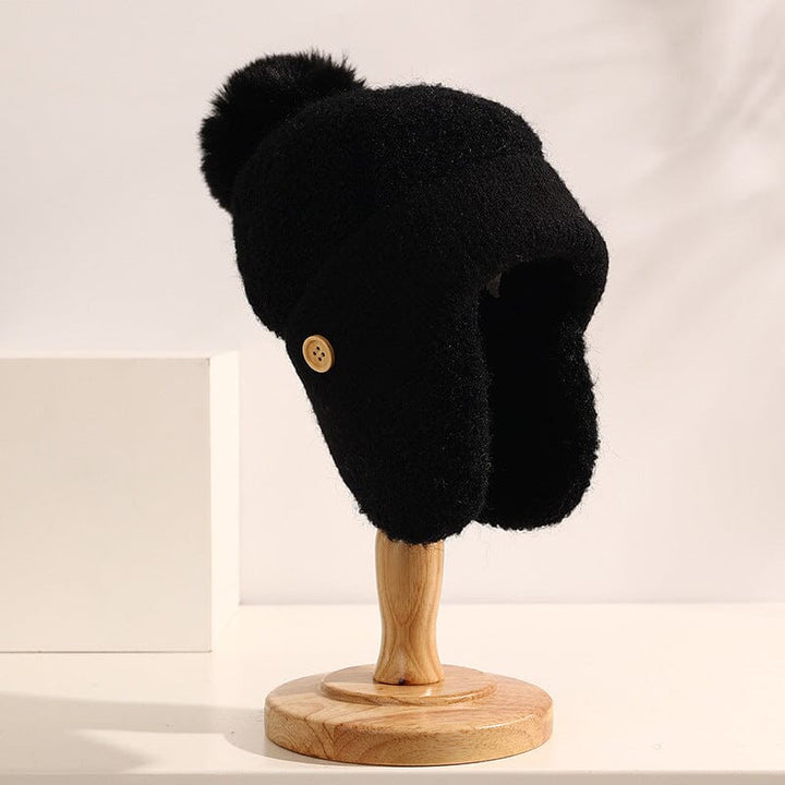 bonnet cache oreille en laine noir pour femme avec pompon et boutons sur support en bois, modèle nina élégant