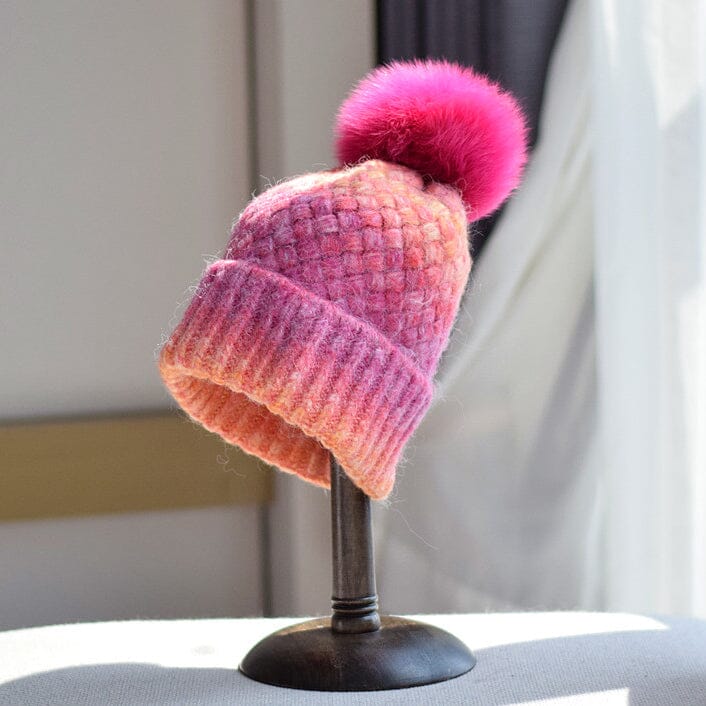 bonnet multicolore en laine avec un pompon rose vif sur un support noir, idéal pour l'hiver et disponible chez Laeticia