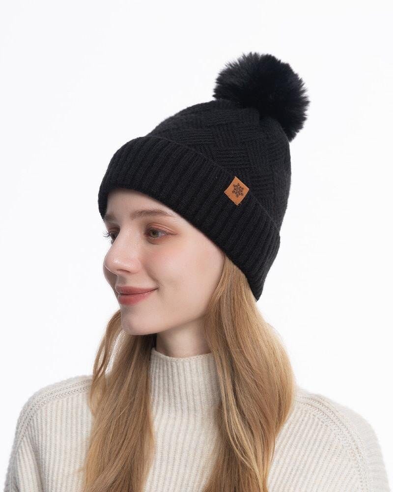 Bonnet en laine noir avec pompon, idéal pour l'hiver, porté avec style par une jeune femme souriante en pull blanc.