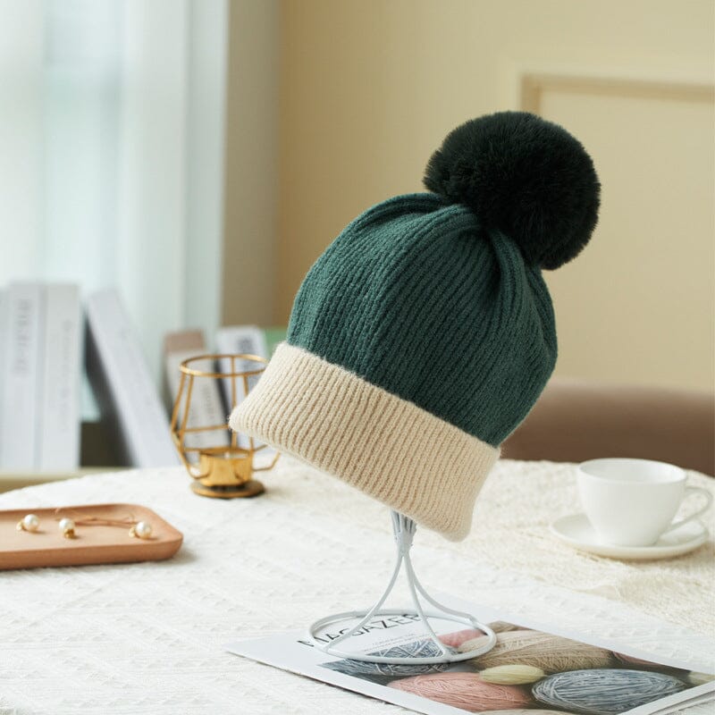 bonnet polaire pauline de couleur vert foncé avec bordure blanche, posé sur une table avec décor cosy en arrière-plan