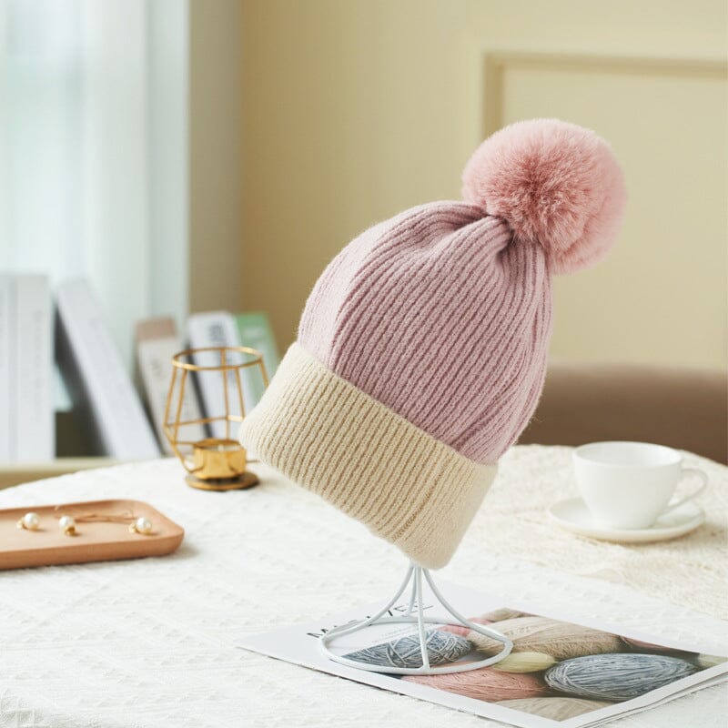 bonnet polaire pauline en laine rose avec pompon, posé sur une table à côté d'une tasse et quelques perles, ambiance cosy