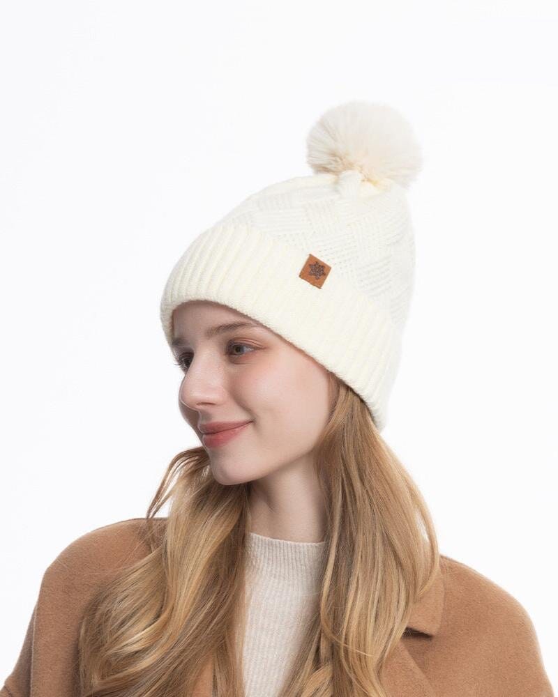 Bonnet en laine blanc avec pompon, modèle Giada nouveauté, porté par une femme souriante en manteau marron.