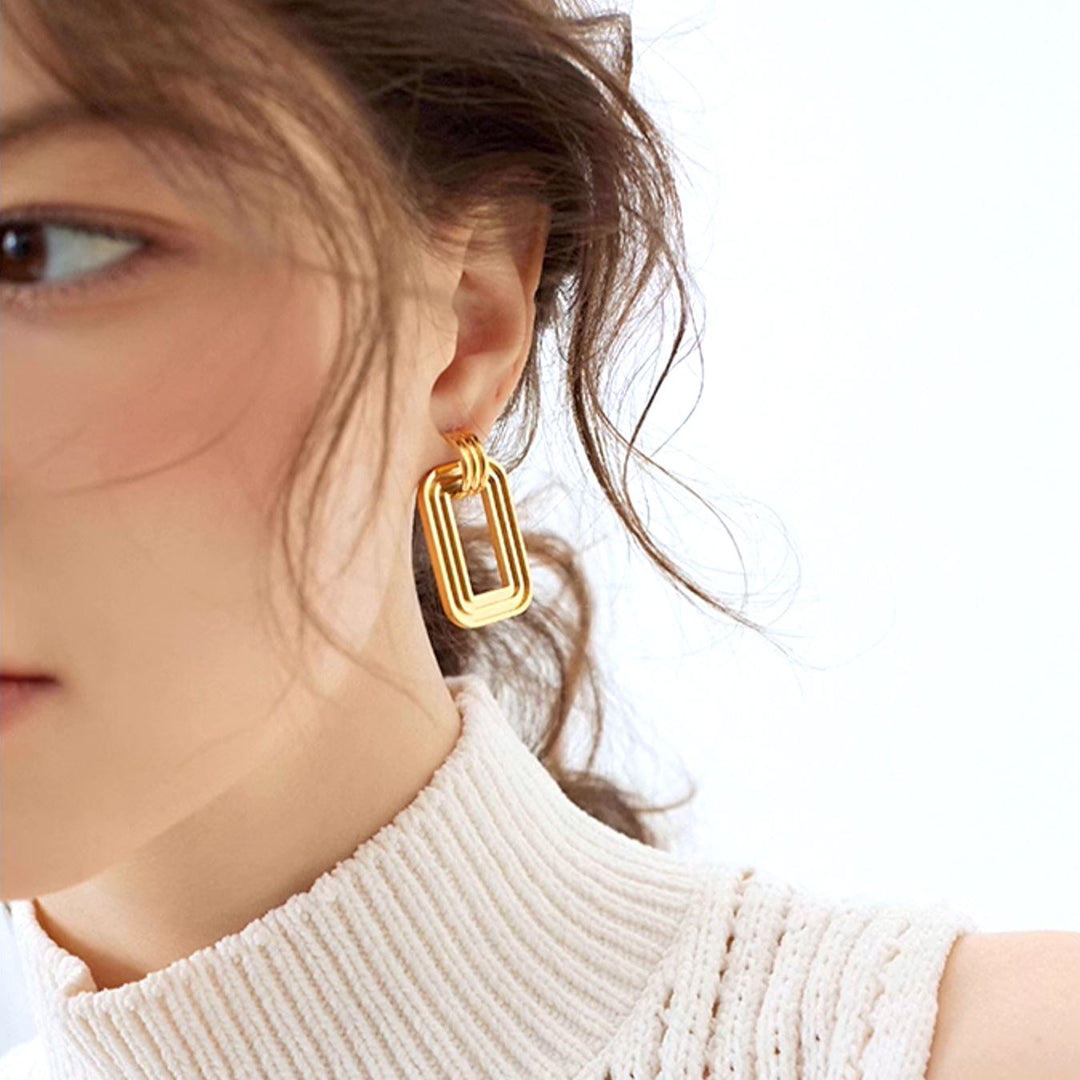 boucles d'oreilles rectangulaires en or portées par une femme, accessoire élégant et moderne pour un look chic