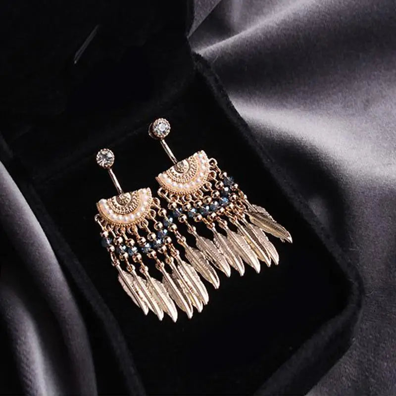 boucles d'oreilles plumes amérindiennes pendantes en métal doré avec des perles noires présentées dans un écrin noir en velours