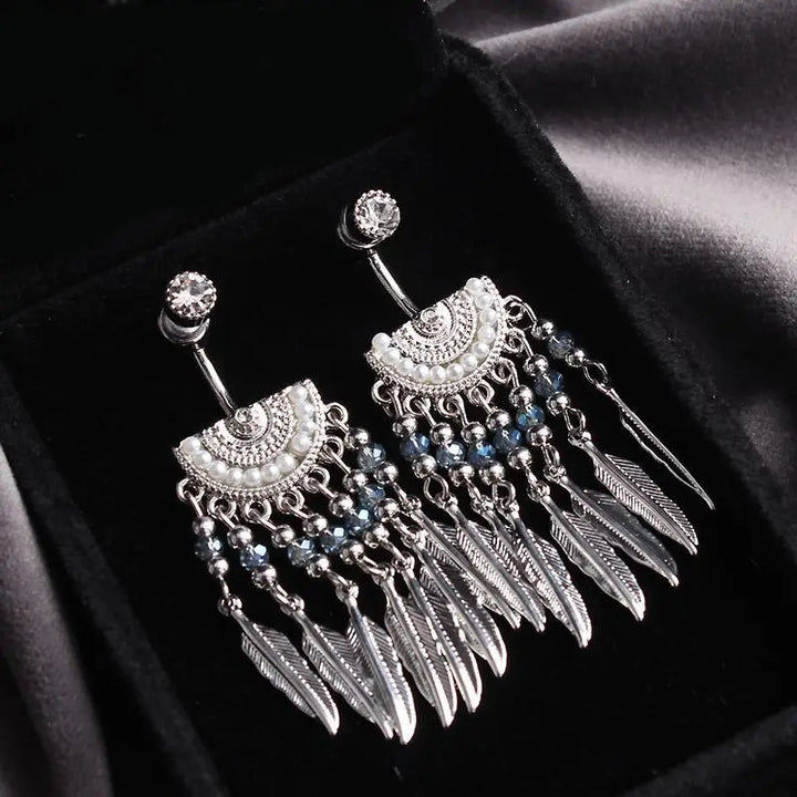 Boucles d'oreilles pendantes argentées avec des perles et des plumes amérindiennes sur fond noir, bijoux élégants et ethniques.