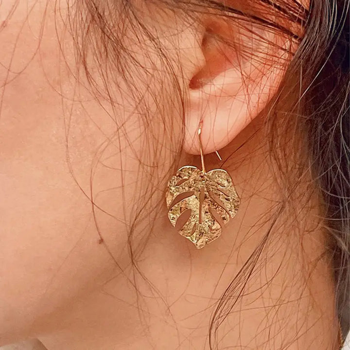 boucles d'oreilles feuille dorée en forme de feuille tropicale portée par une femme, style naturel et élégant