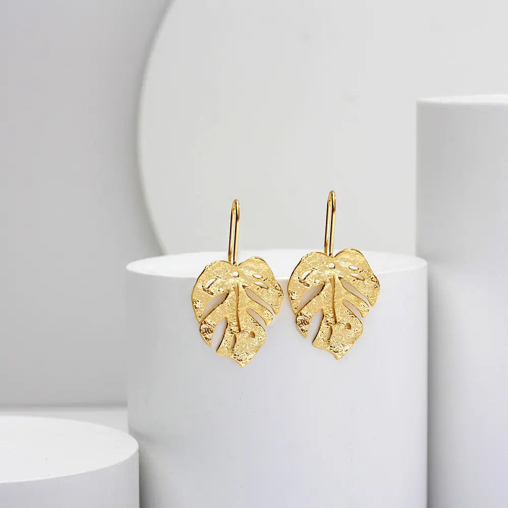 boucles d'oreilles en forme de feuille dorée, élégantes et délicates, mises en avant sur un fond minimalist