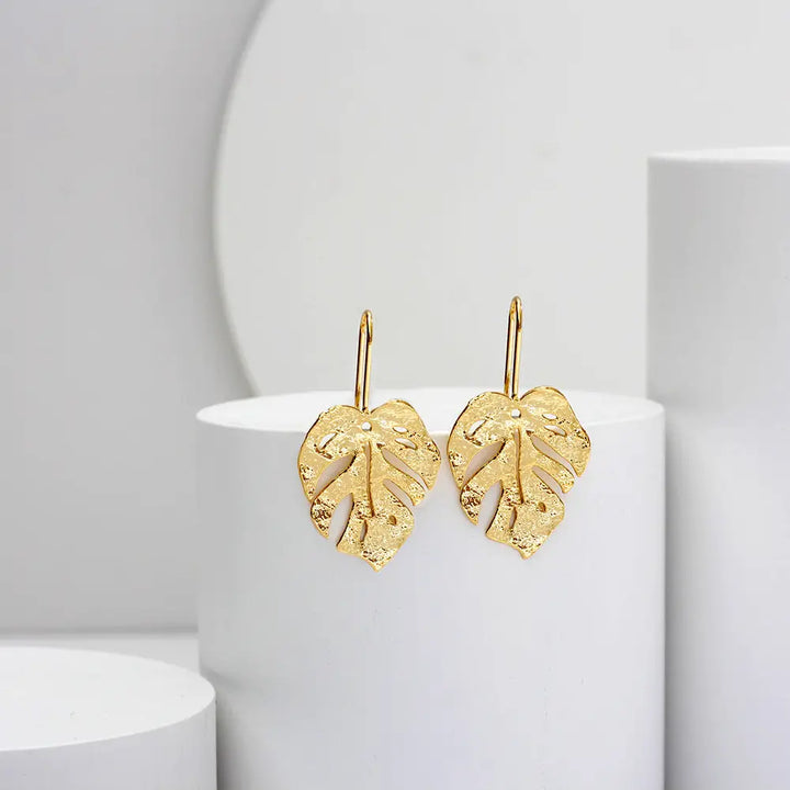 boucles d'oreilles en forme de feuille dorée, élégantes et délicates, mises en avant sur un fond minimalist