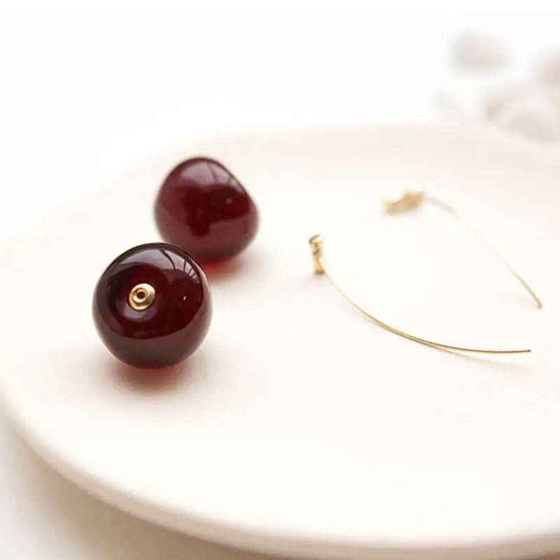 boucles d'oreilles en forme de cerise avec monture dorée sur assiette blanche