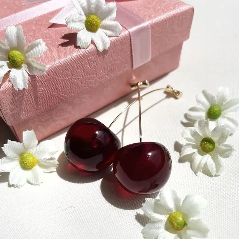boucles d'oreilles cerise avec fleurs blanches près d'une boîte rose élégante, accessoire de mode féminin charmant