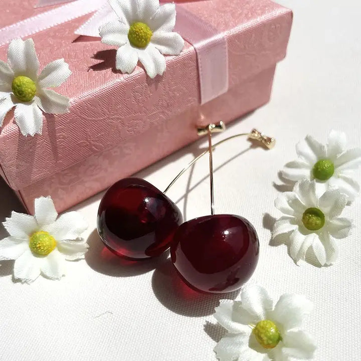 boucles d'oreilles cerise avec fleurs blanches près d'une boîte rose élégante, accessoire de mode féminin charmant
