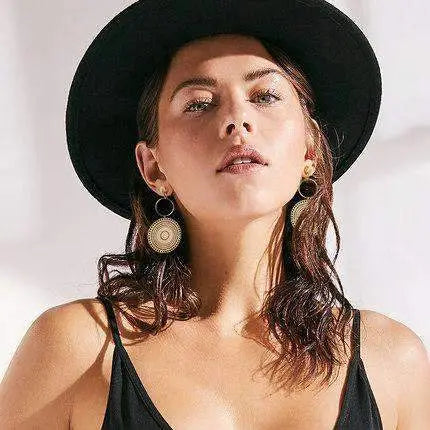 boucles d'oreilles ethniques chics en forme de soleil portées par une femme avec un chapeau noir et une robe noire