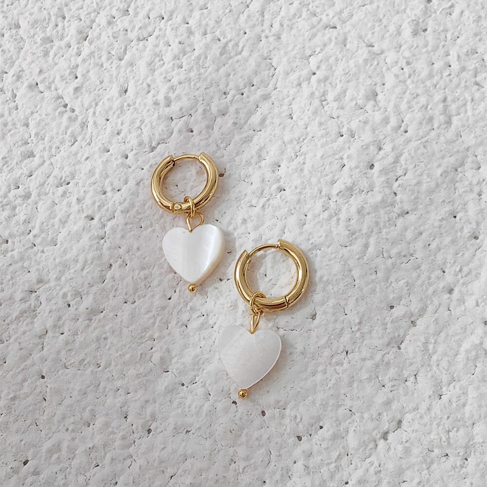 boucles d'oreilles en forme de cœur avec pendentifs nacrés irma élégantes et raffinées sur fond blanc texturé