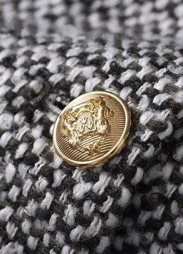 Détail élégant d'une veste en tweed pour femme ornée d'un bouton doré, style chic et intemporel pour tenues habillées.