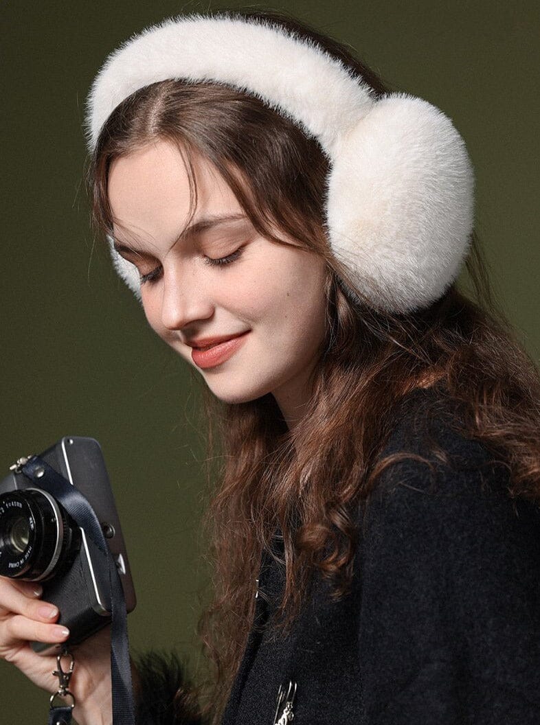 jeune femme portant un cache-oreilles en fausse fourrure blanche tout en tenant un appareil photo retro et souriant