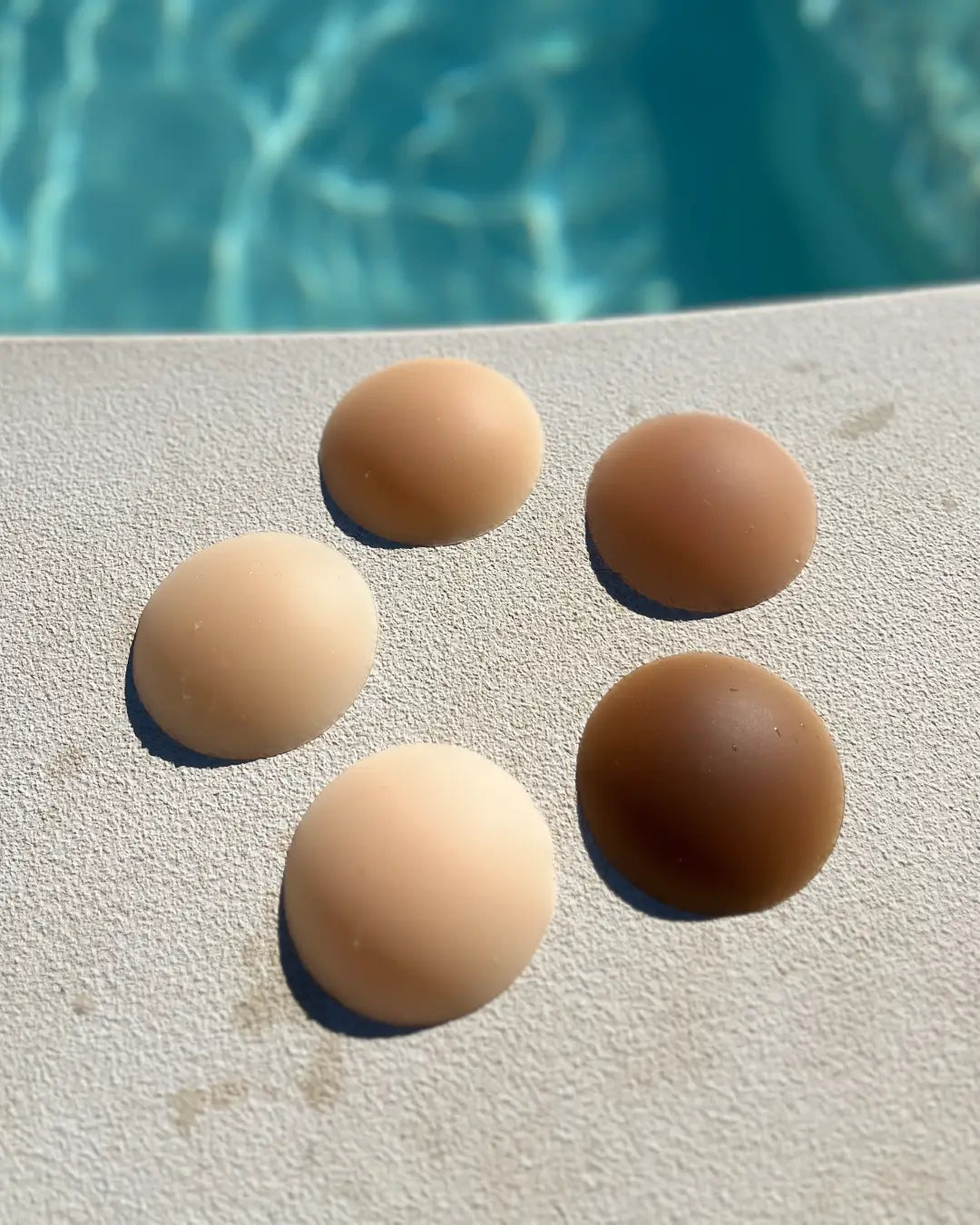 Cache-tétons en silicone discrets et sans adhésif, disponibles en plusieurs teintes sur fond près de la piscine.