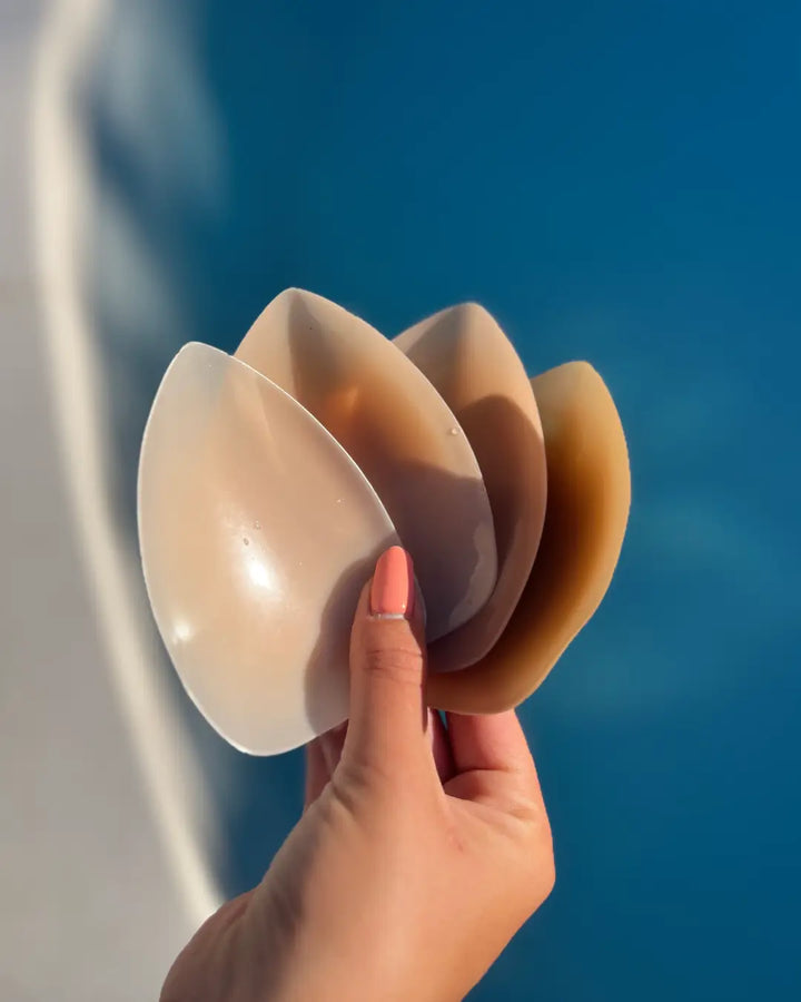 Cache-tétons sans adhésif, forme triangulaire en silicone, tenus par une main au-dessus d'un fond bleu.