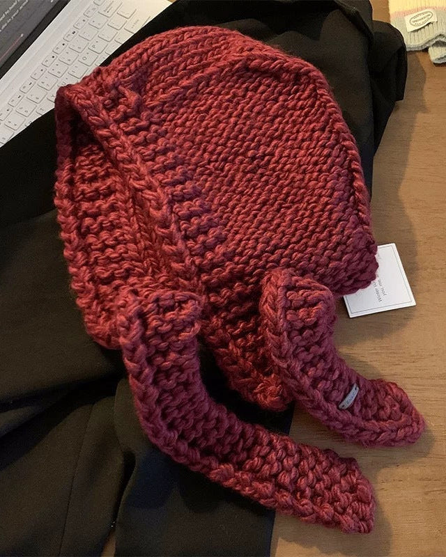 Écharpe cagoule en grosse maille rouge pour l'hiver, tendance et confortable, vue sur une table en bois foncé.