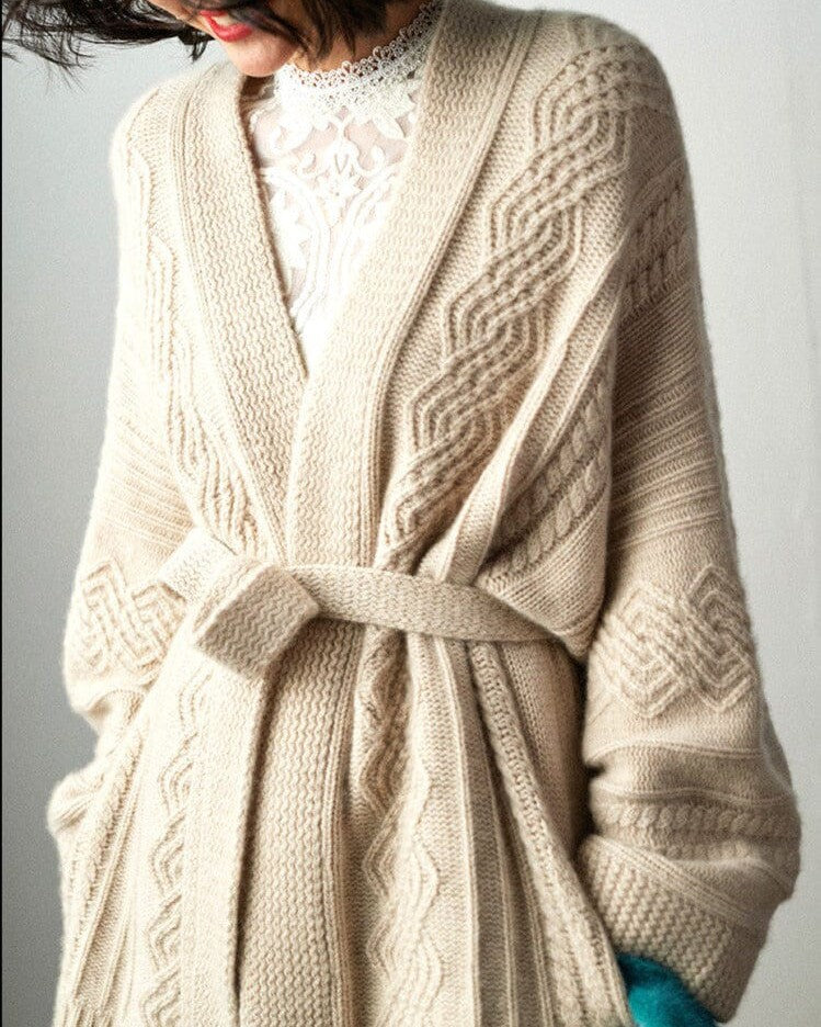 cardigan ceinturé beige en maille avec motifs torsadés porté par une femme avec un haut en dentelle blanche