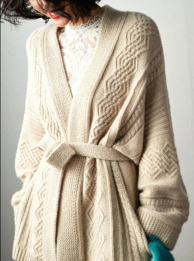 cardigan ceinturé beige en maille avec motifs torsadés porté par une femme avec un haut en dentelle blanche