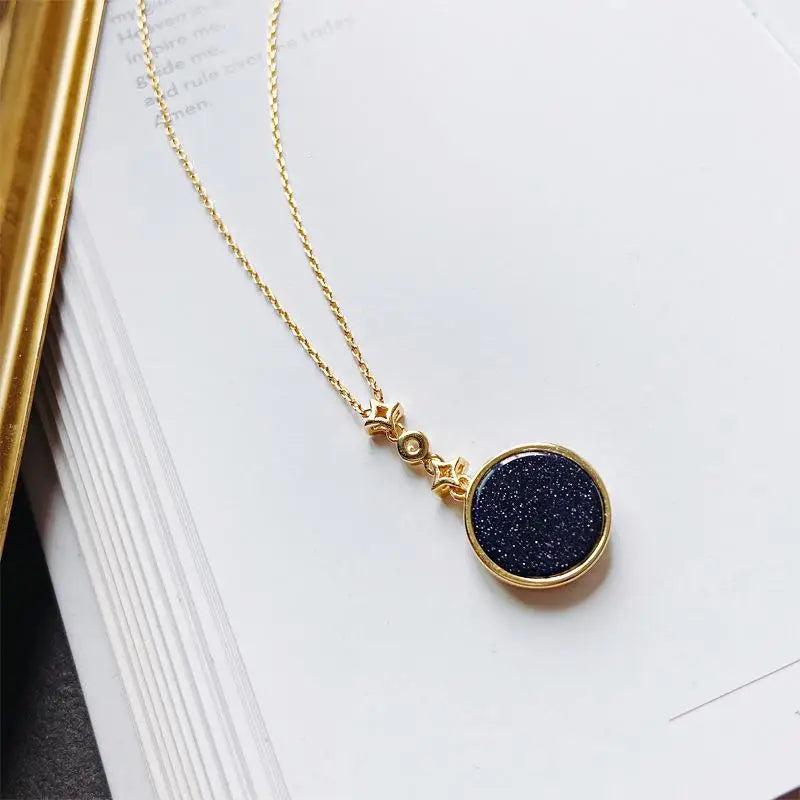 collier médaillon féminin en or avec motif cycle lunaire et ciel étoilé sur fond de livre blanc et couverture dorée