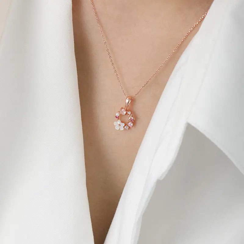 collier pendentif en or rose en forme de couronne avec des fleurs élégantes porté par une personne sur un fond blanc