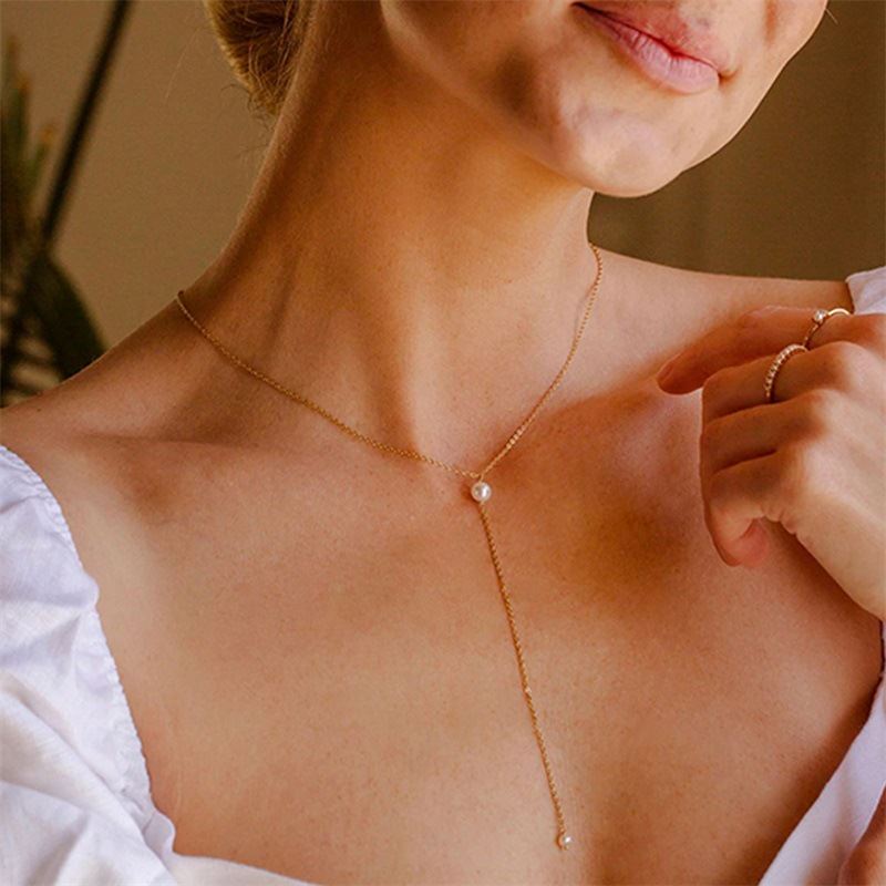 collier en or avec perle blanche pendante sur le décolleté d'une femme, accessoire chic et élégant nommé caroline